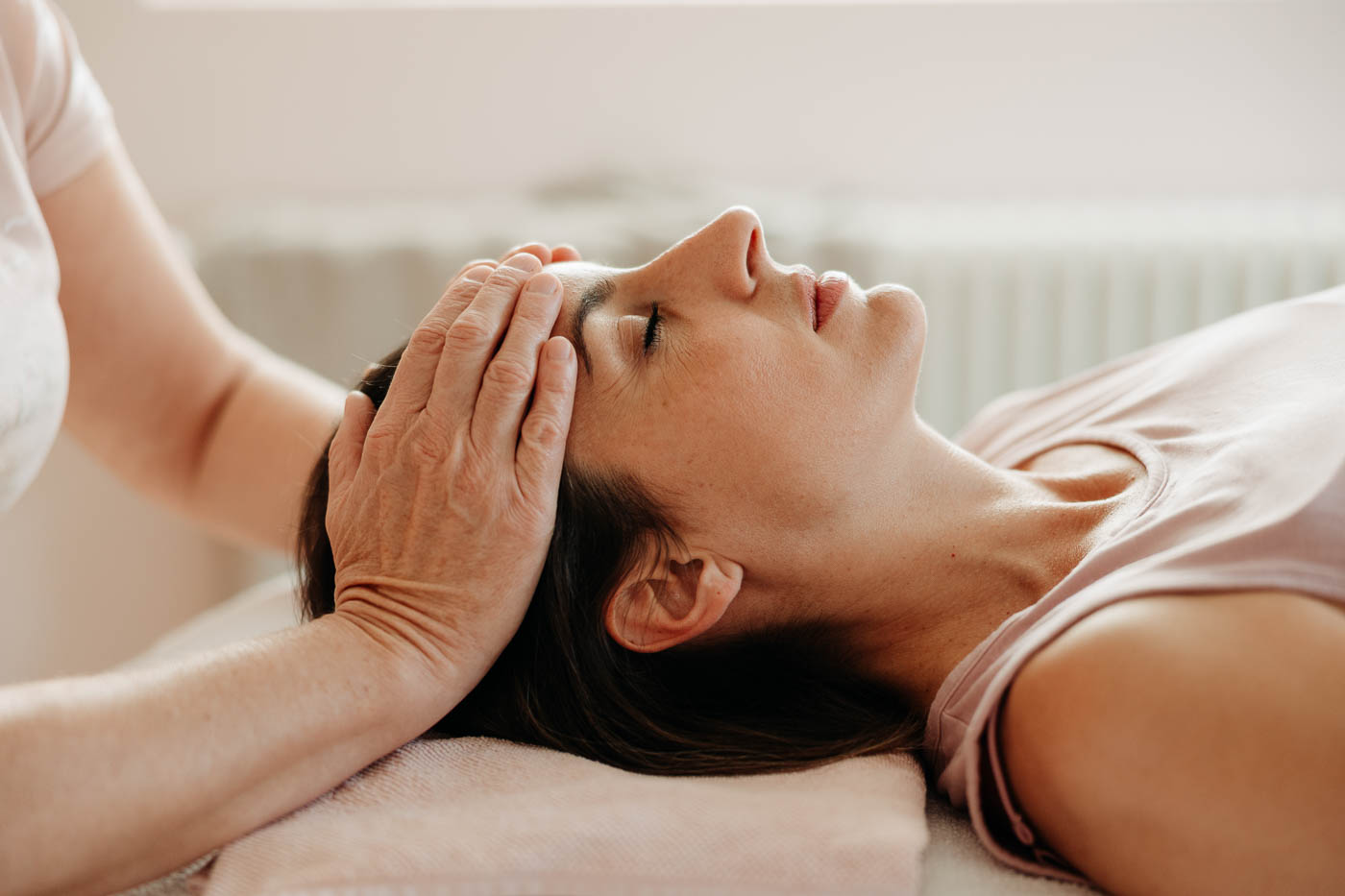 Eine Frau liegt auf dem Rücken, zwei Hände liegen sanft auf ihrer Stirn