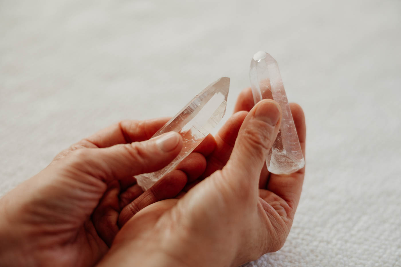 Zwei Hände, jede Hand hält einen stiftförmigen Bergkristall